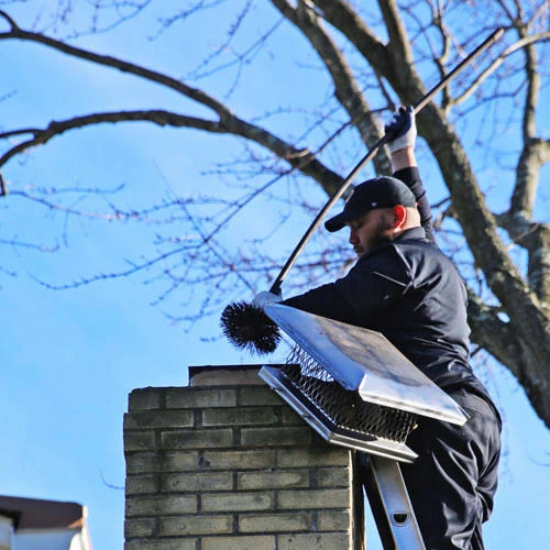 Person using a chimney brush beside a removed metal chimney cap