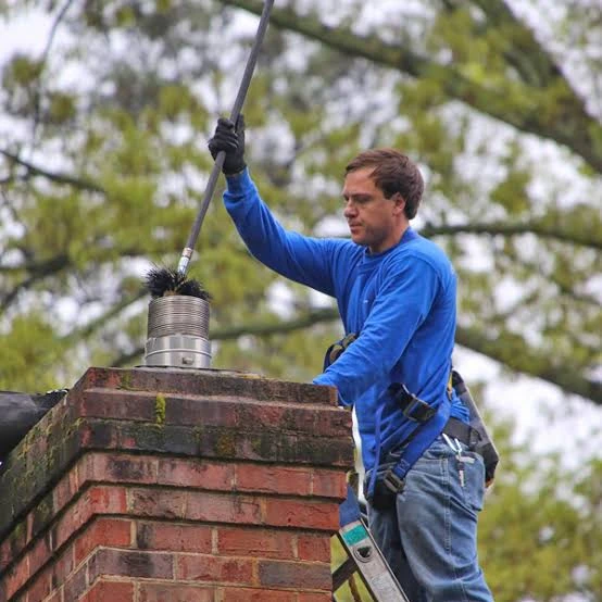 Person brushing a metal flue opening above a brick chimney