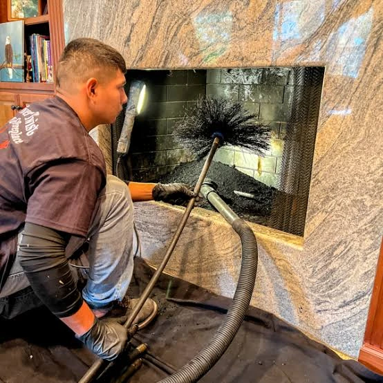 Person cleaning a dark firebox with a round brush and vacuum hose