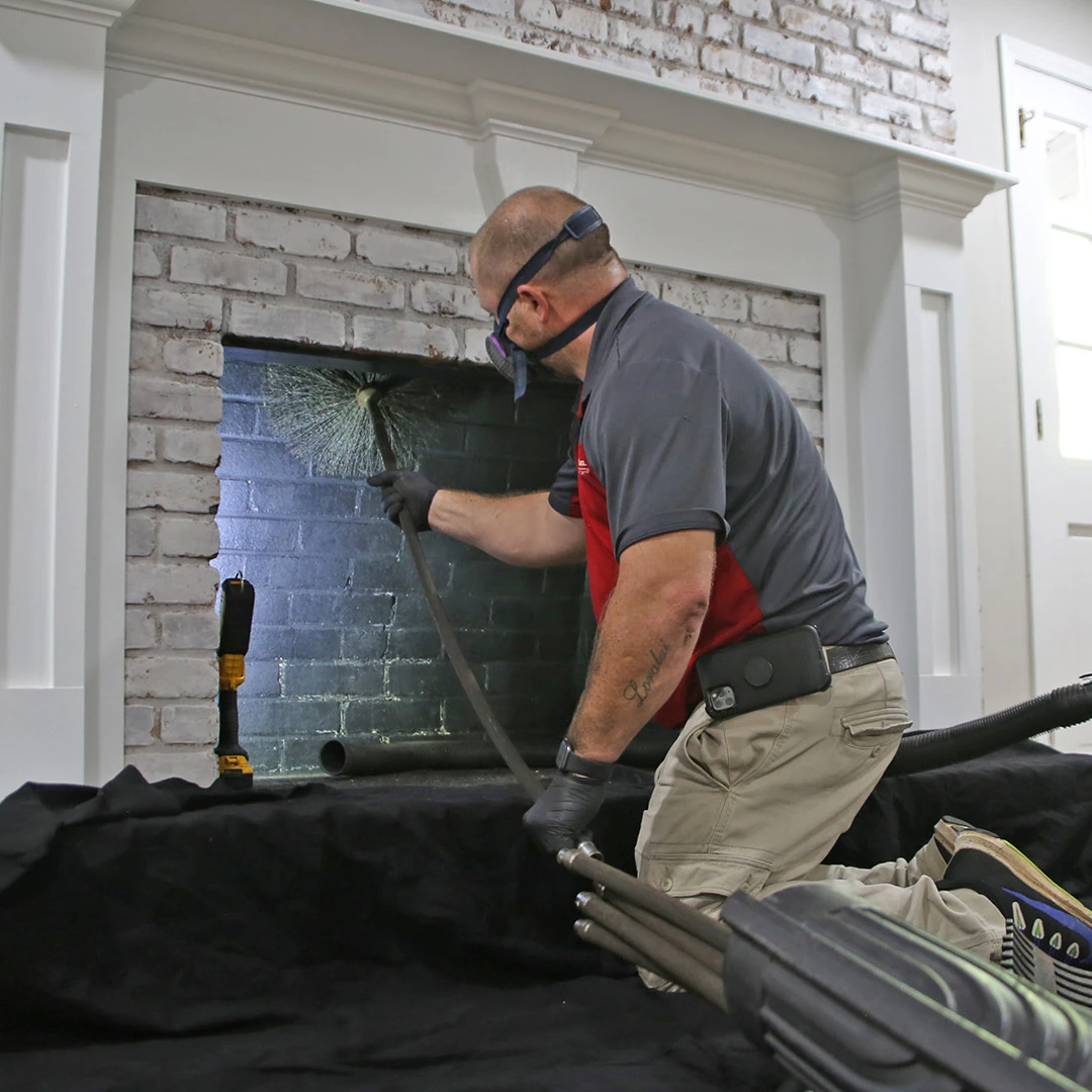 Person using a chimney brush inside a white brick fireplace