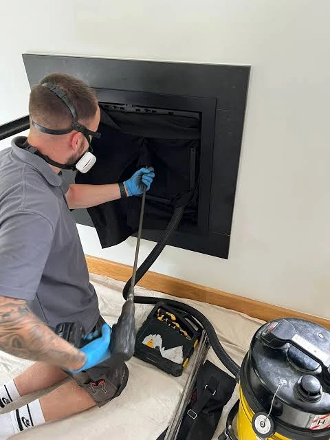 Person cleaning a modern black fireplace insert with a vacuum hose