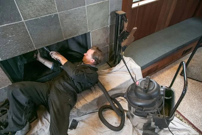 Person cleaning the interior of a fireplace with protective floor coverings and vacuum equipment