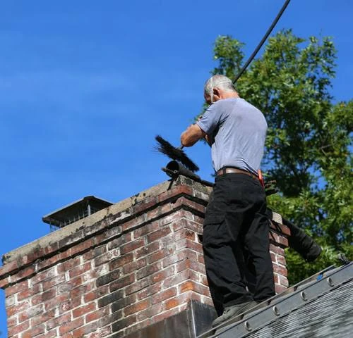 Person working with a brush beside a masonry chimney on a pitched roof